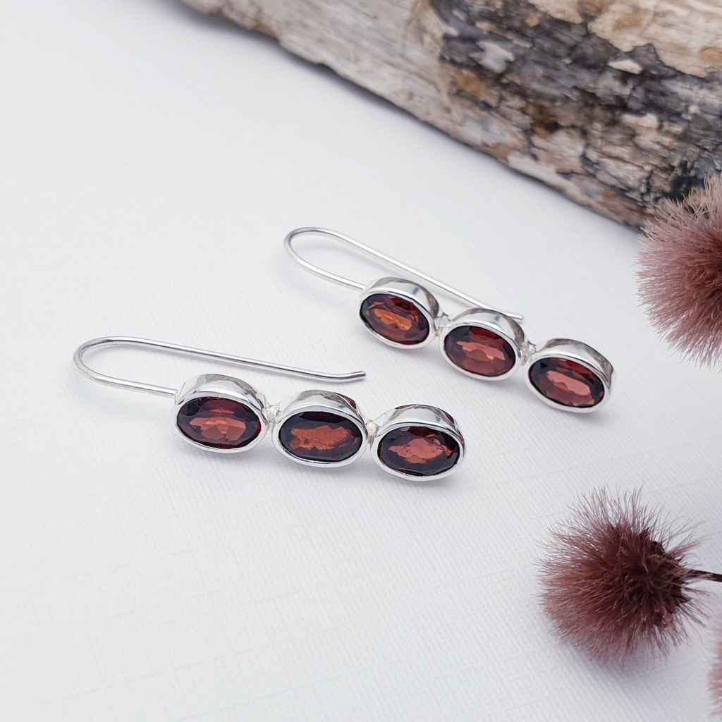 Our Garnet Orla earrings displayed against a white background with bark and flowers as decorations
