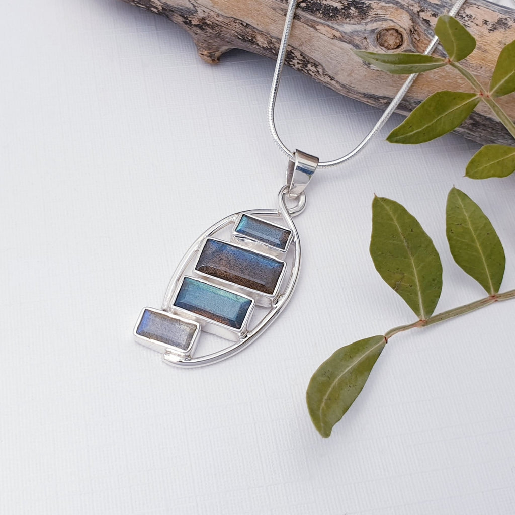 Our Labradorite rectangles pendant pictured against white with driftwood and leaves as decoration