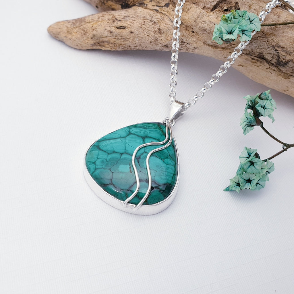 Our Malachite pan pendant pictured against white with driftwood and green flowers in the background as decoration