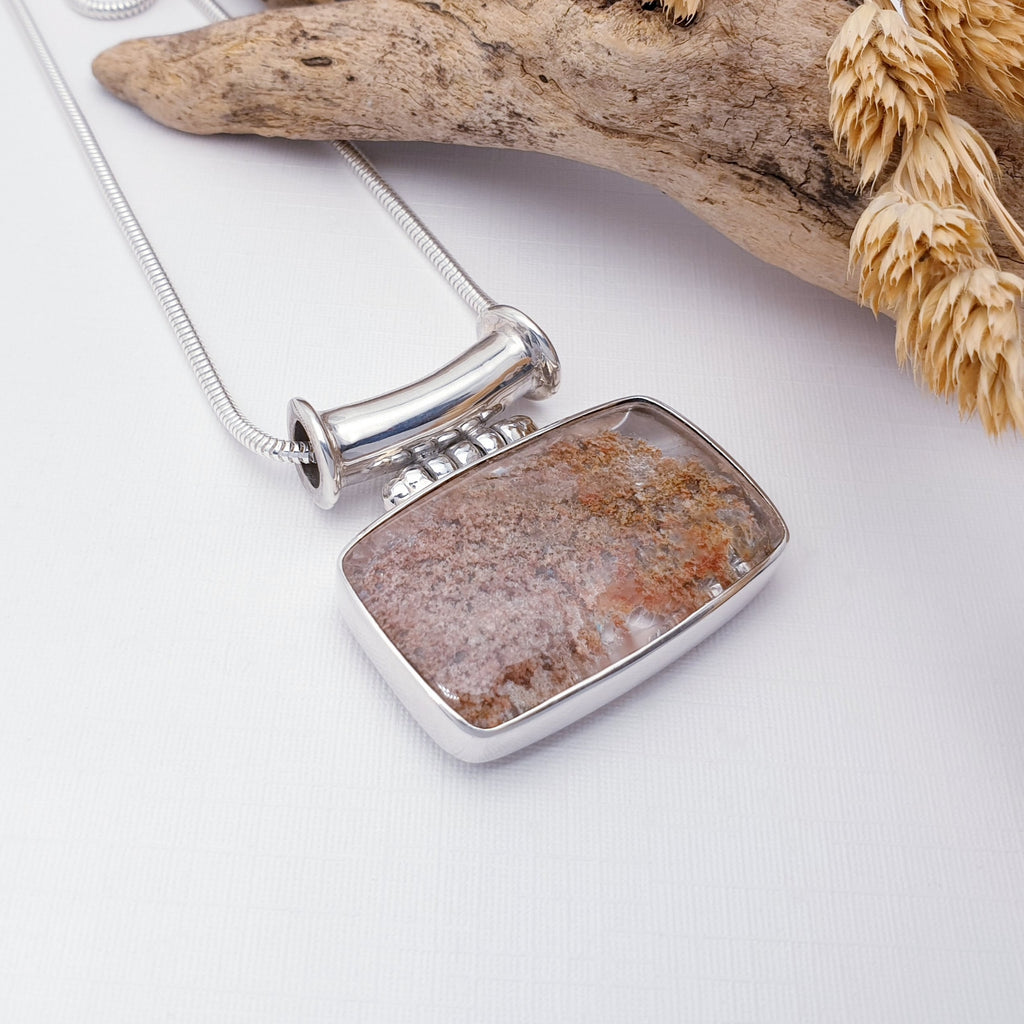 Our one off Lodolite helios pendant pictured against white with driftwood in the background as decoration