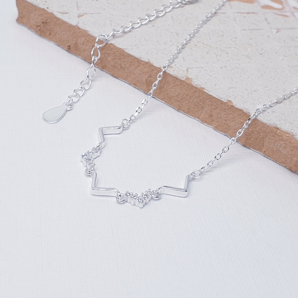 Our cubic zirconia dainty necklace pictured against white and laid out on a tile