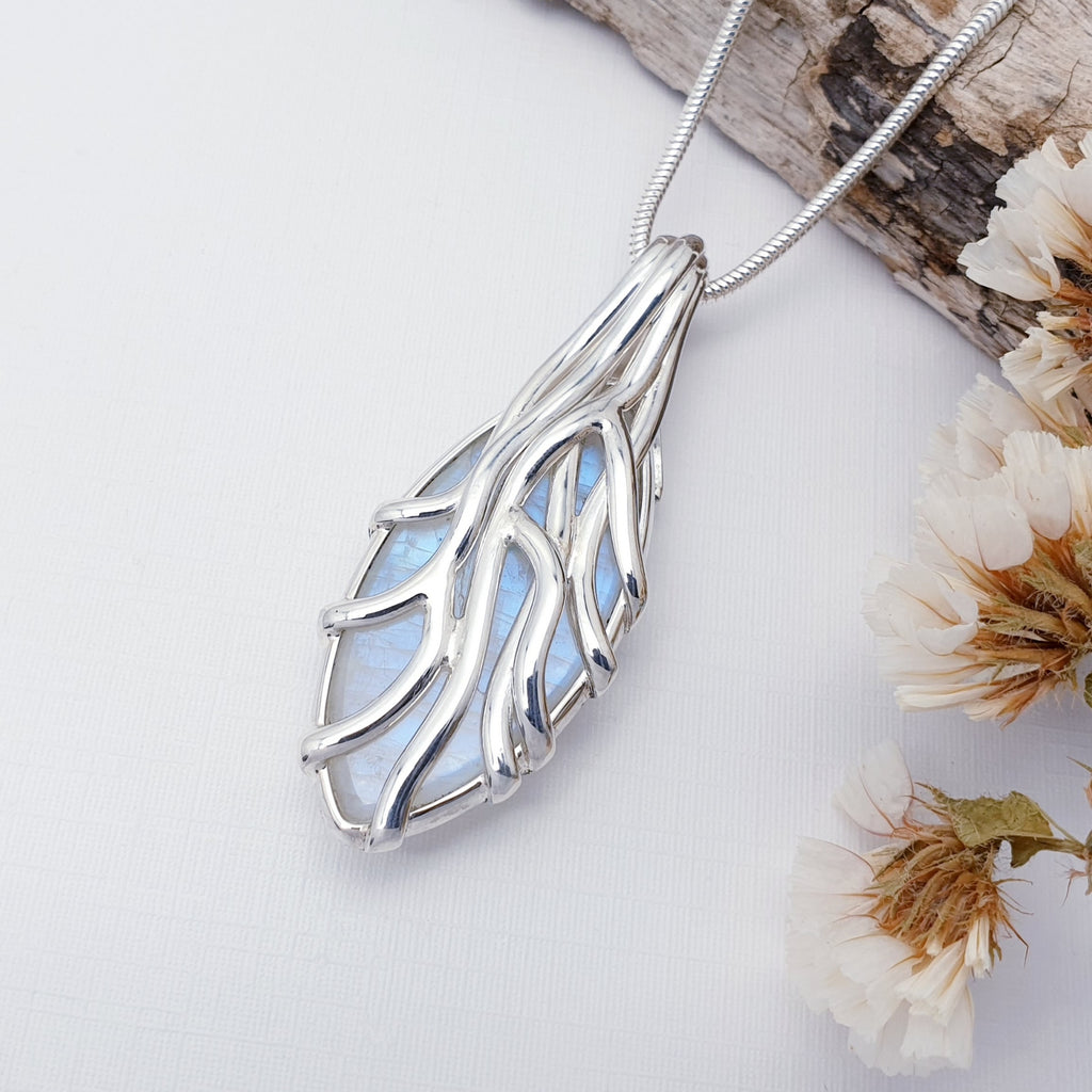 Silver leaf-shaped Moonstone pendant on a white background with dried flowers.