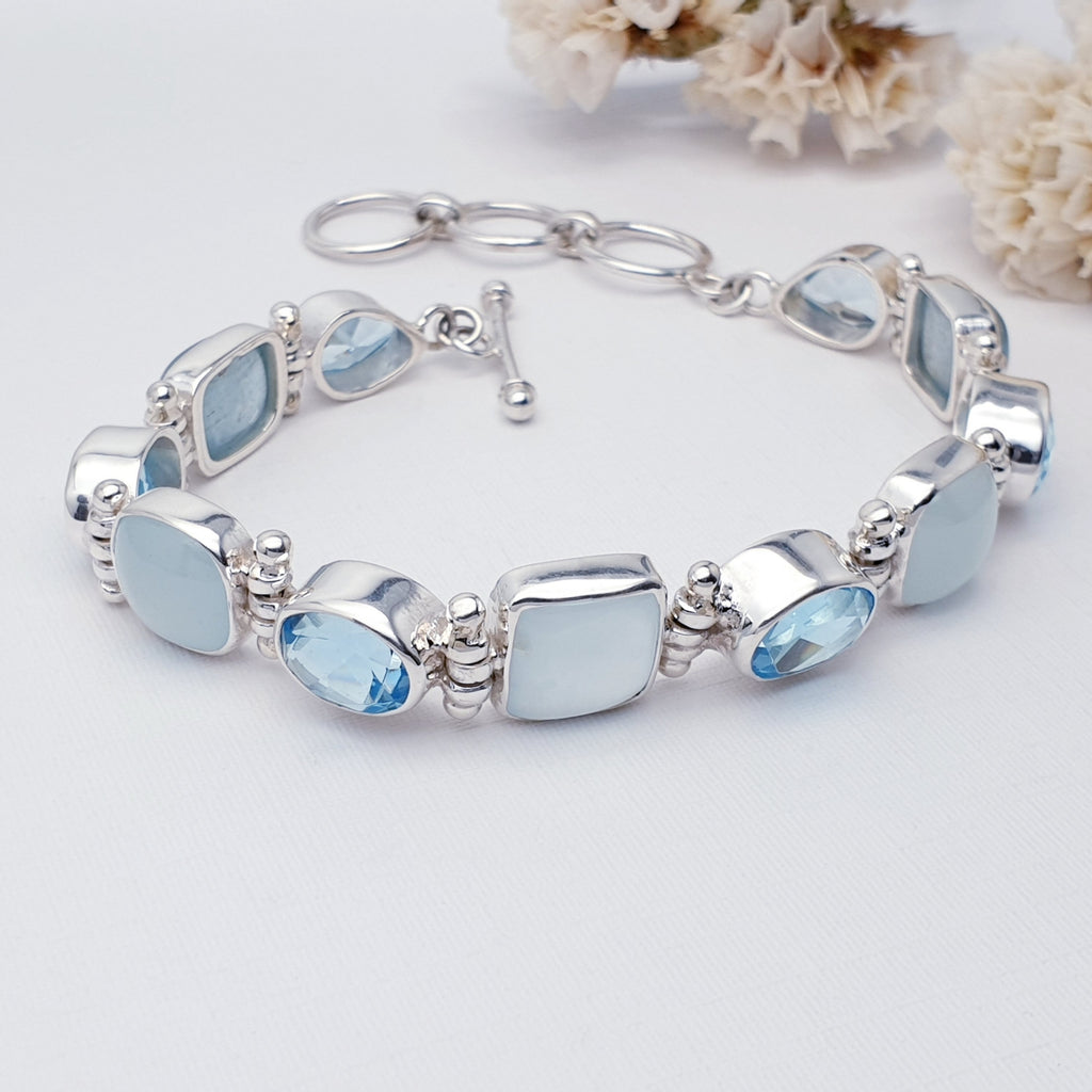 Aquamarine and Blue Topaz bracelet on a white background with petals in the top right corner