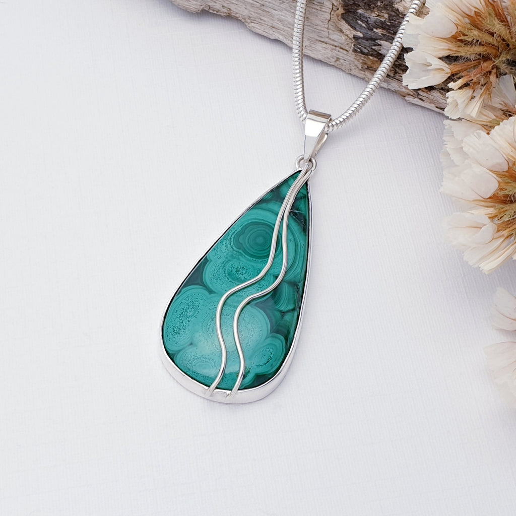 Our one of a kind Malachite Pan pendant pictured against white with driftwood and dried flowers in the background.