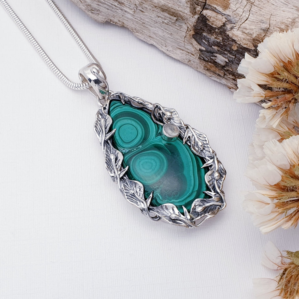 Malachite and Moonstone pendant on a white background with wood and petals as decorations
