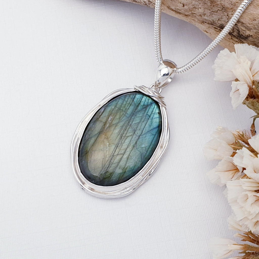 Silver pendant with a labradorite stone on a white background with dried flowers.