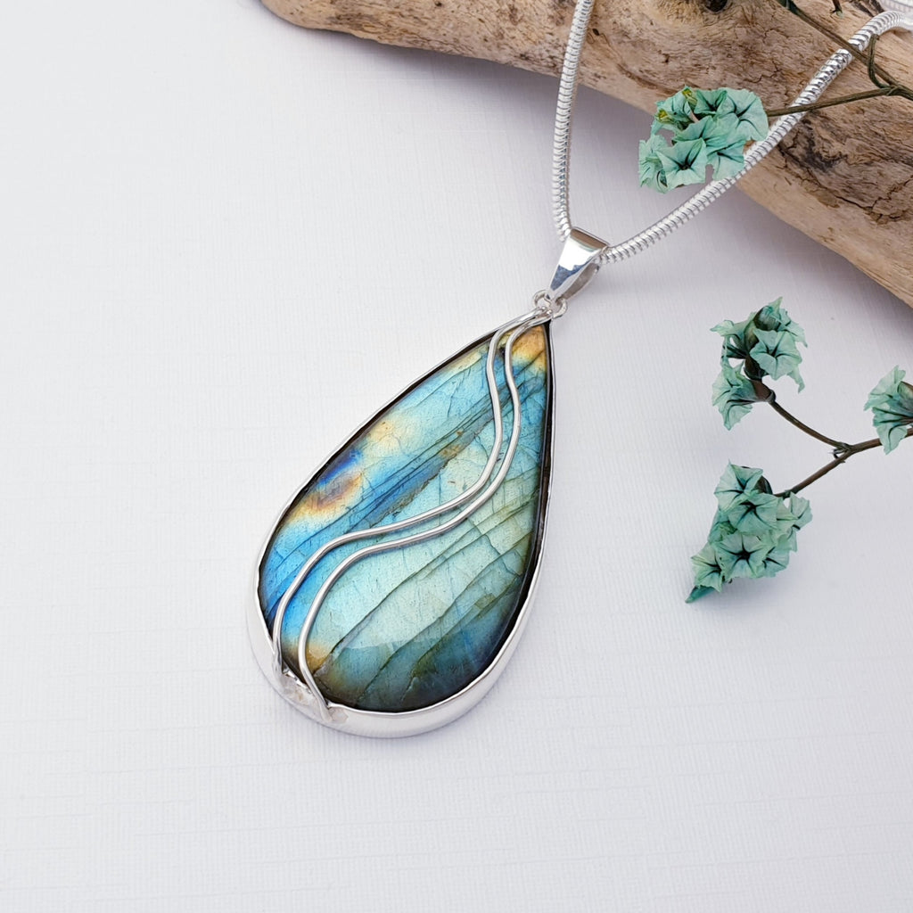 Labradorite pendant on a white background with wood and dried flowers as decorations