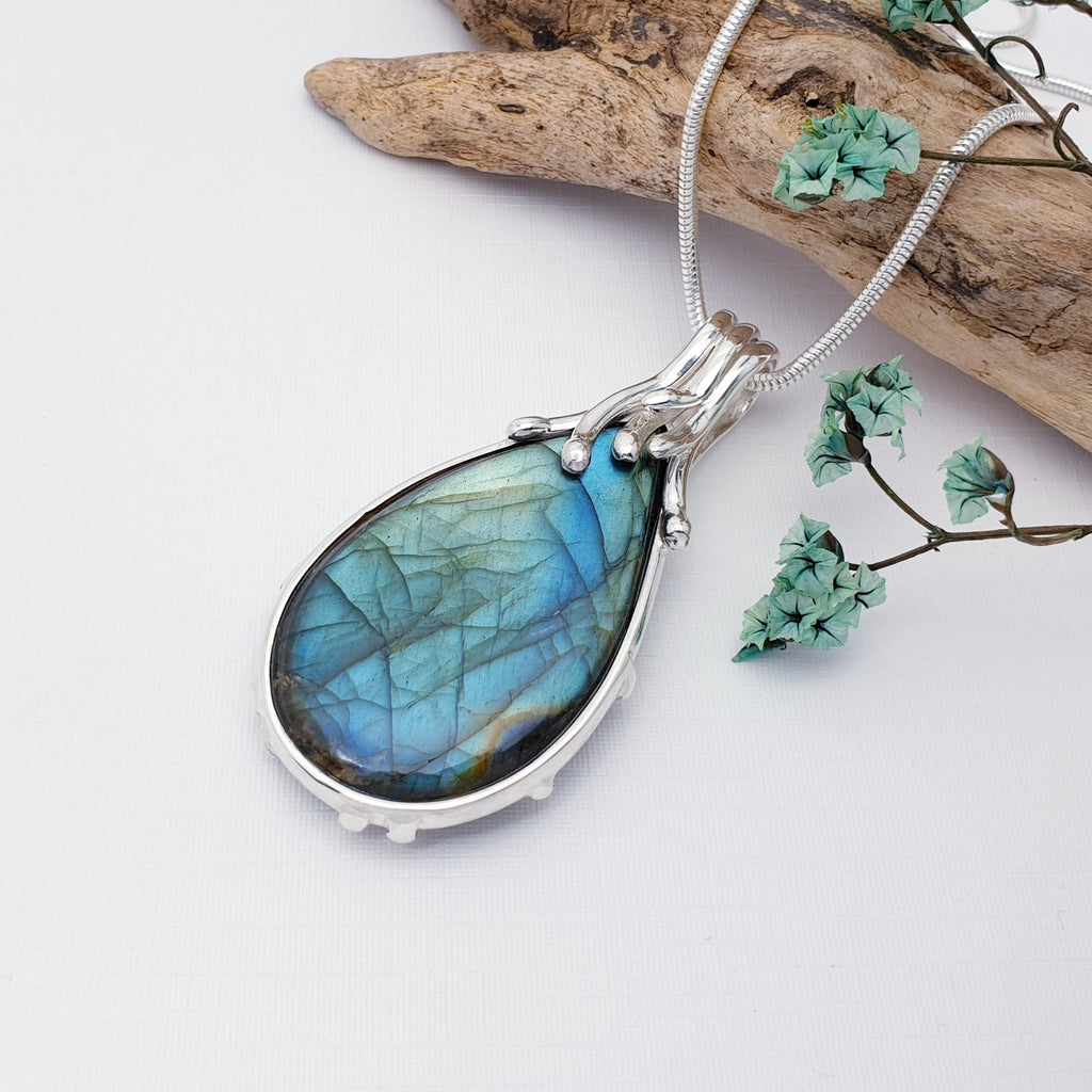 Labradorite reversible pendant on a white background with a piece of wood and petals in the top right corner