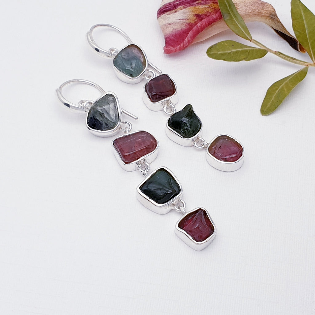 Tourmaline earrings on a white background with leaves and petals in the top right corner
