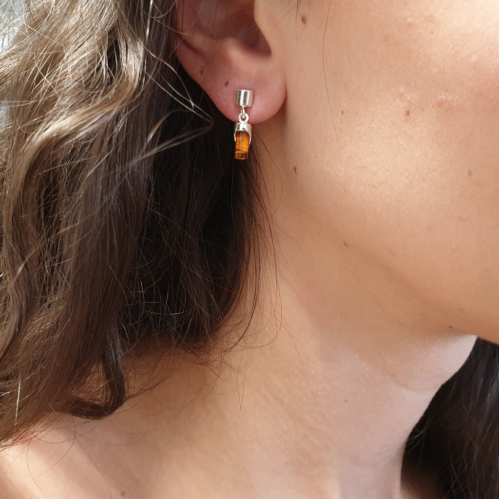 A model wearing one cylindrical amber and sterling silver earring.
