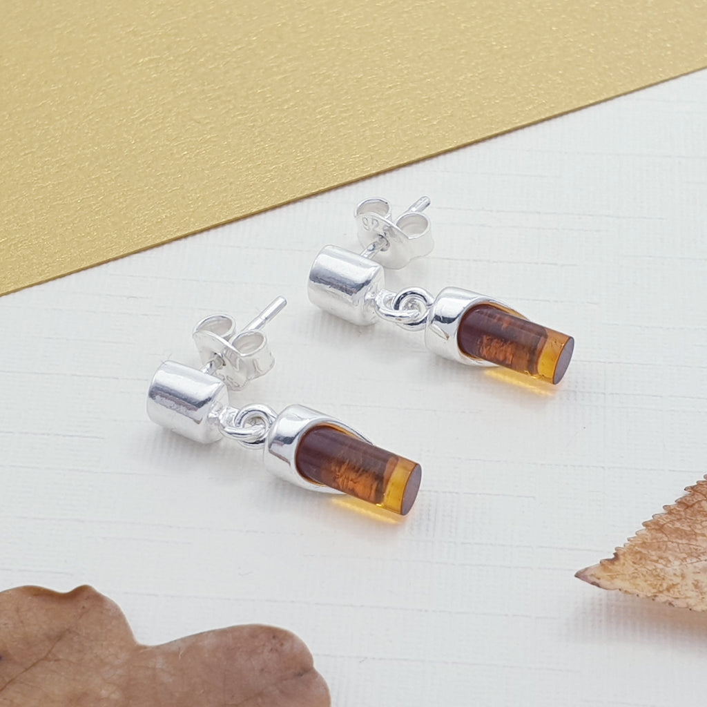 A pair of cylindrical amber and sterling silver earrings with autumn foliage.