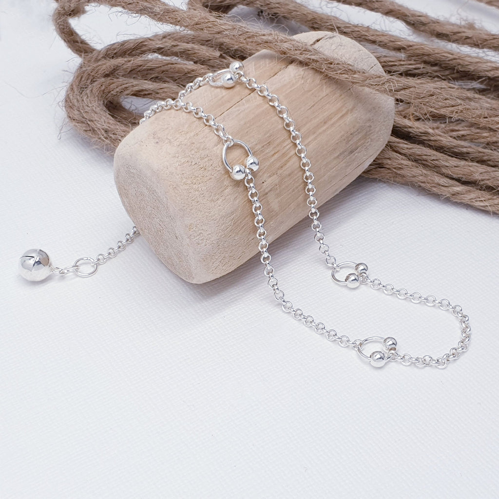 A simple design featuring five Sterling Silver circles and two small Silver balls, that delicately hang from the bottom of each circle. In between the circles a belcher chain completes this summer beachwear accessory. As a finishing touch, a Silver bell has been added to the end of the extension chain.