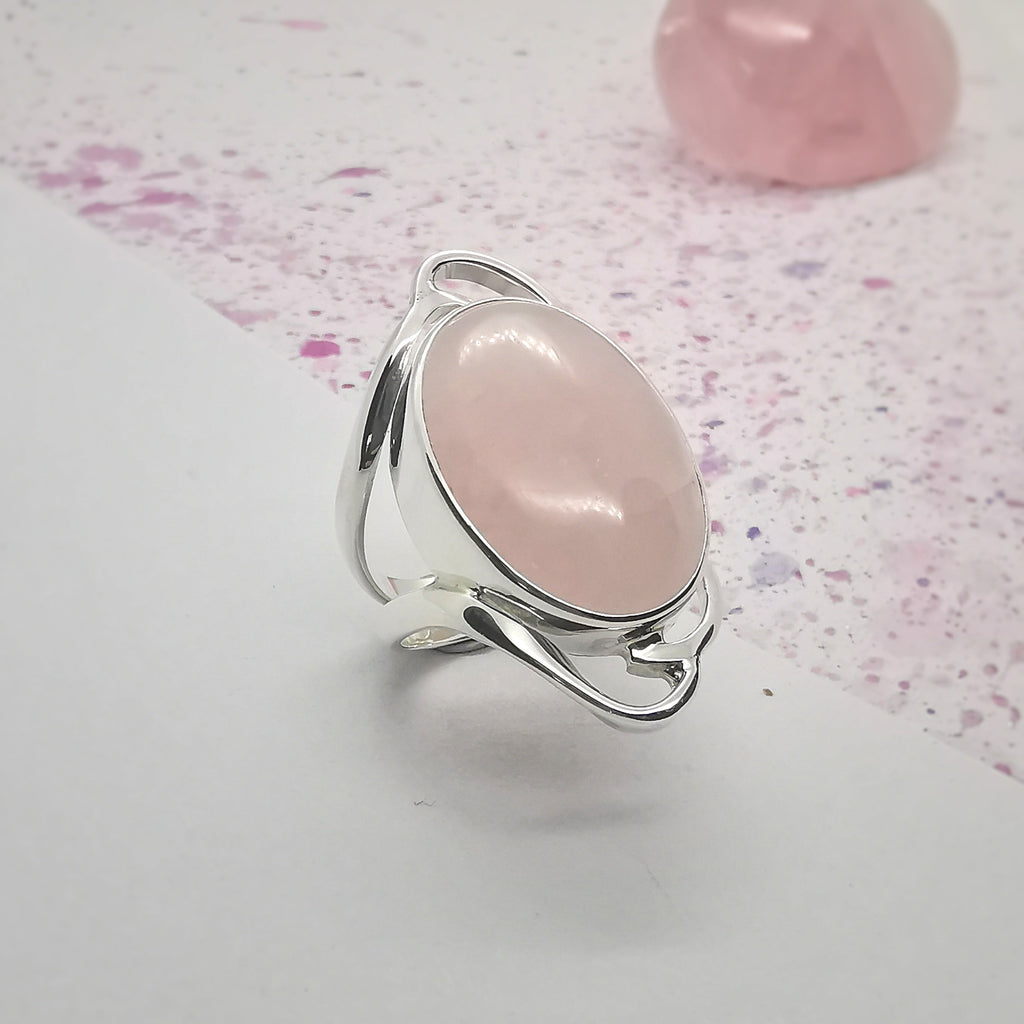 This gorgeous statement ring features a large, oval, cabochon, Rose Quartz stone. The beautiful stone is showcased by a simple Sterling Silver swirl design that decorates the top and bottom of the ring. 