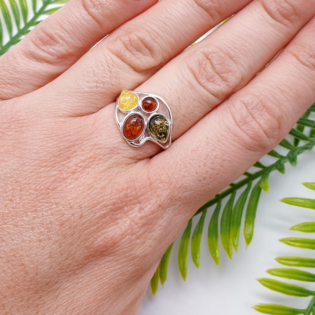 This ring features two Baltic Toffee Amber stones; one oval and a smaller round stone sitting below, both in simple settings. Two more Amber stones; one yellow and one green teardrop shapes, beautifully finishes off the face of the ring. A simple Sterling Silver swirl design decorates the top and bottom of the ring. 