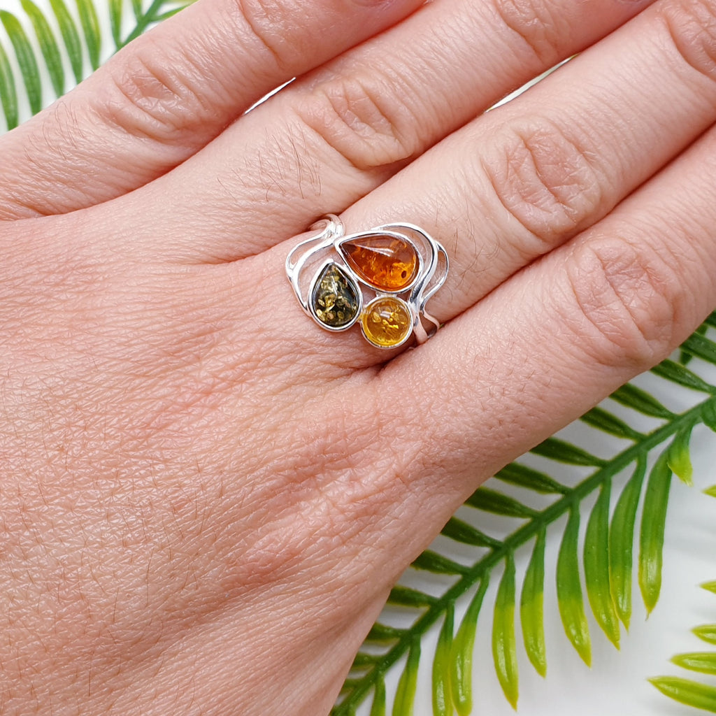 This ring features three Baltic Amber stones; two teardrop Toffee and green stones, and one round yellow Amber stone. The three Amber stones are showcased by a simple Sterling Silver wave design that decorates the top and bottom