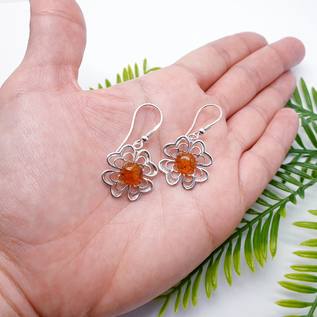 Each earring features a round beautiful Toffee Amber stone. Showcasing the Amber stone is a Sterling Silver flower cut out design. The intricate flower detailing creates an unusual design, these earrings are perfect for any occasion. 