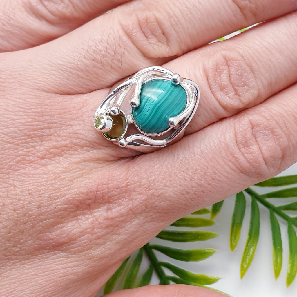 This ring features a gorgeous free form Malachite stone and above sits a beautiful oval tabletop Peridot stone. Showcasing the fabulous stones our silversmiths have created a nature inspired design of Silver 'creeping vines'.  A Sterling Silver fine wire swirl, with a stunning tiny table top Peridot stone on the end, decorates the top of the stone, completing the design.