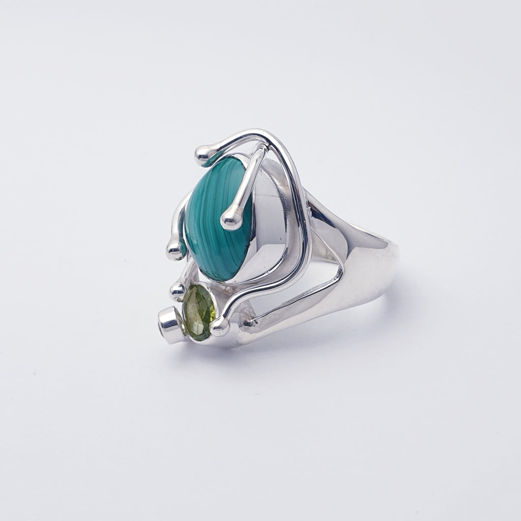 This ring features a gorgeous free form Malachite stone and above sits a beautiful oval tabletop Peridot stone. Showcasing the fabulous stones our silversmiths have created a nature inspired design of Silver 'creeping vines'.  A Sterling Silver fine wire swirl, with a stunning tiny table top Peridot stone on the end, decorates the top of the stone, completing the design.