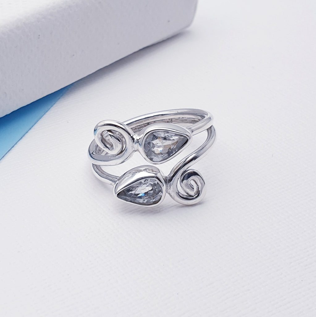 This beautiful ring features two tabletop cut, teardrop shaped Aquamarine stones in Sterling silver settings. Our silversmiths have created an elegant swirl shape design that give this ring that 'something a little different' we love so much at Silver Scene.