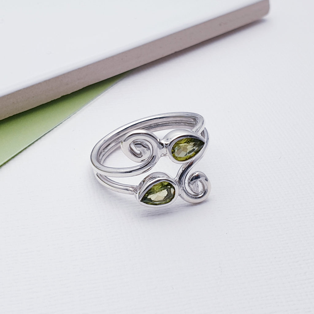 This beautiful ring features two tabletop cut, teardrop shaped Peridot stones in Sterling Silver settings. Our silversmiths have created an elegant swirl shape design that give this ring that 'something a little different' we love so much at Silver Scene.