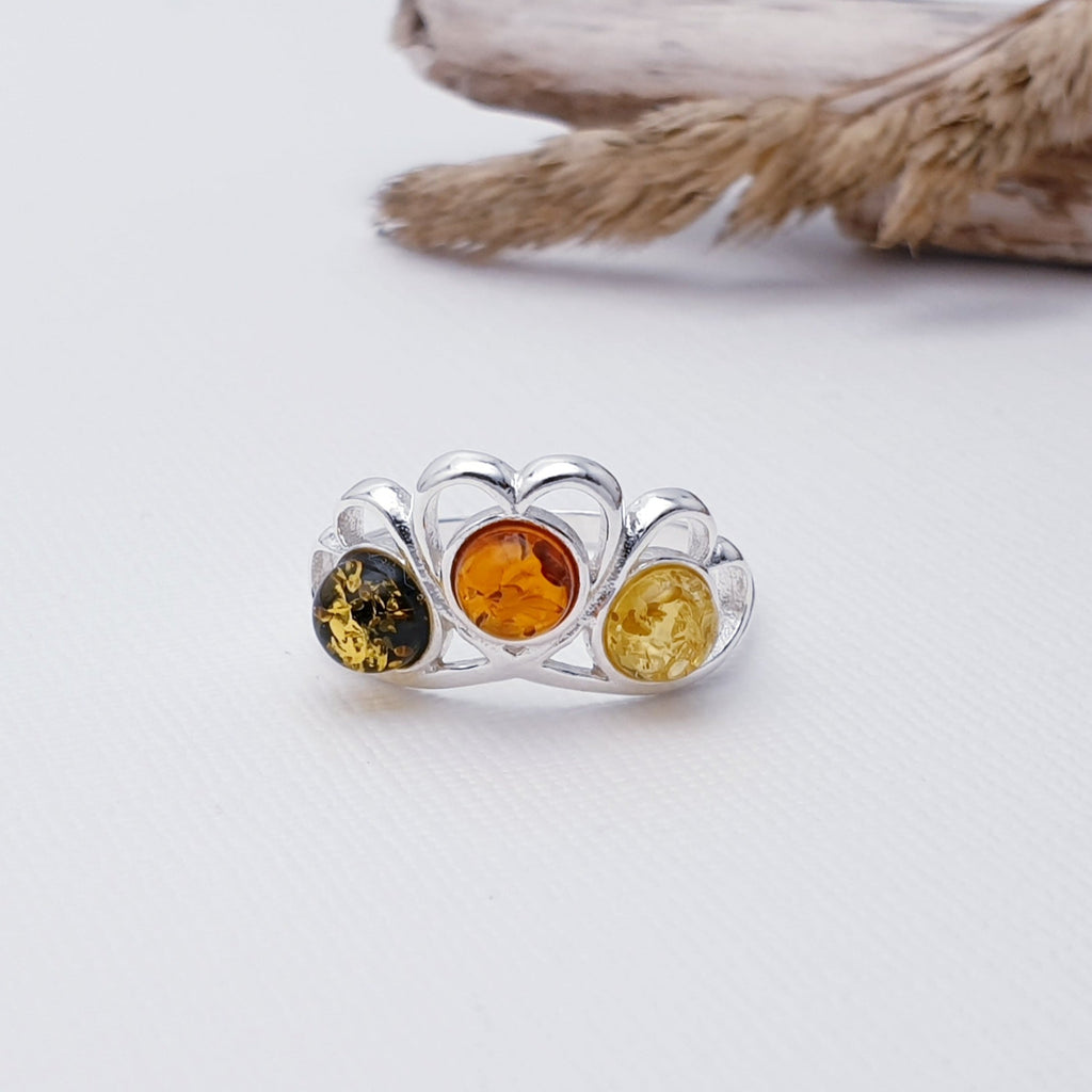 This ring features three round Mixed Amber stones; one green, one Toffee and one yellow in simple settings. Above each stone Sterling Silver heart detailing decorates the top of the ring.