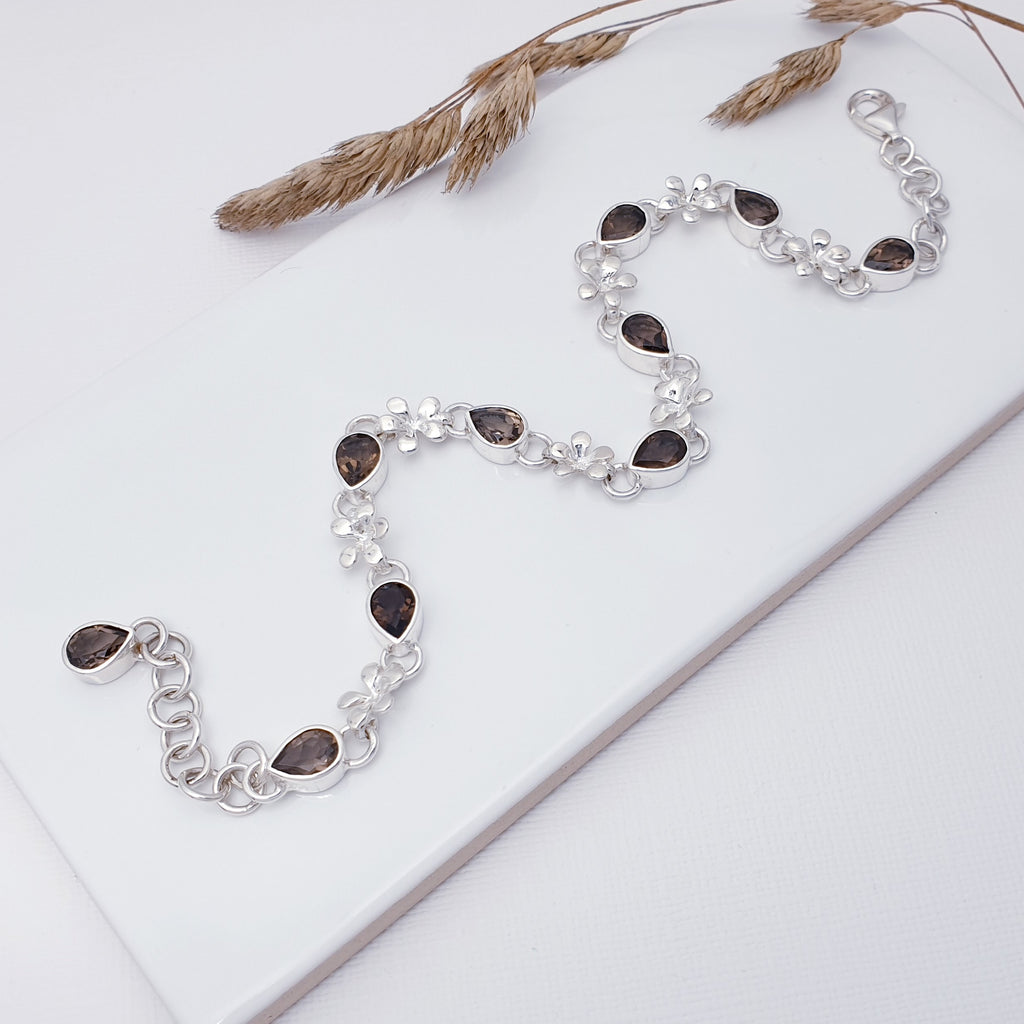 This bracelet features nine teardrop, tabletop cut, Smoky Quartz stones in simple settings, plus one more beautiful Smoky Quartz stone at the end of the extension chain. Decorative Sterling Silver flower links attach each stone to the next, creating a simple yet elegant bracelet. The extendable chain on the end gives you peace of mind when buying as a gift, as it can be worn in lengths 8" to 9.5", the perfect length for larger wrists.