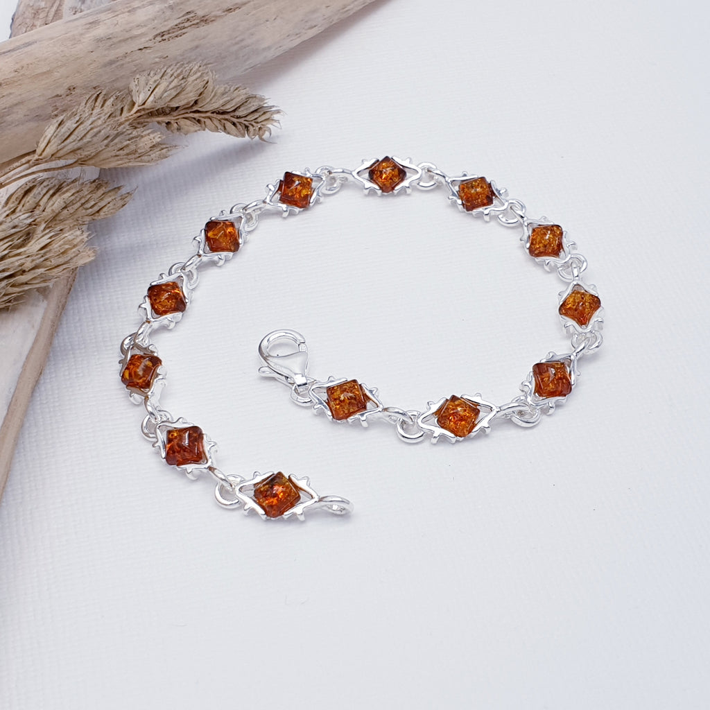 This simple bracelet features thirteen square Baltic Toffee Amber stones in simple Sterling Silver settings.  Decorative Silver triangle shapes links attach each stone to the next creating an contemporary and fluid design.