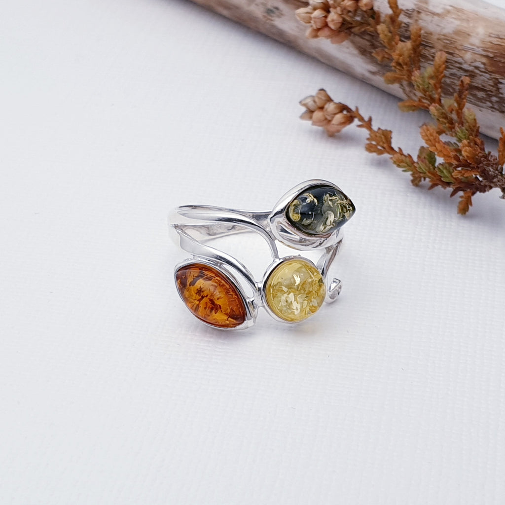This ring features three Baltic Amber stones; two marquise Toffee and green stones, and one round yellow Amber stone. A simple Sterling Silver whirl design decorates the side and wraps delicately around the finger.