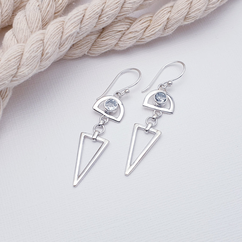 A simple yet eye catching design, each earring features a round tabletop cut, Blue Topaz stone in simple settings. Surrounding the stone our silversmiths have added a Sterling Silver semi-circle that showcase the stones beautifully. As a finishing touch, a triangle drops down from the bottom.