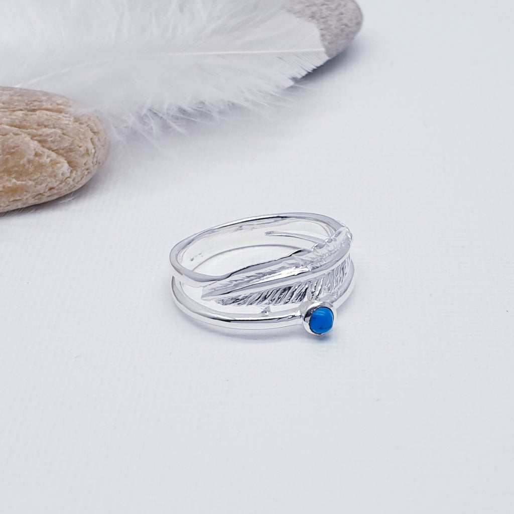 A beautiful design, this ring features a stunning cabochon, round, Turquoise stone in a simple setting. Above the stone is a gorgeous feather, with an 'icing sugar' finish and gorgeous detailing. Two silver bands are fused together at both ends creating an interesting design.