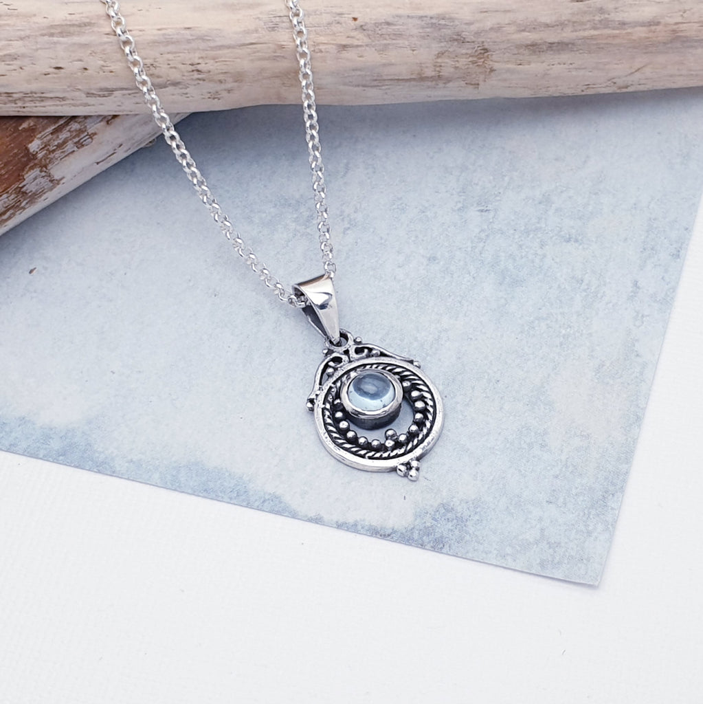 A gorgeous design, this pendant features a round, cabochon Blue Topaz stone in a simple setting. Intricate Sterling Silver detailing decorates around the stone, and is given depth and presence by the clever use of oxidisation. 
