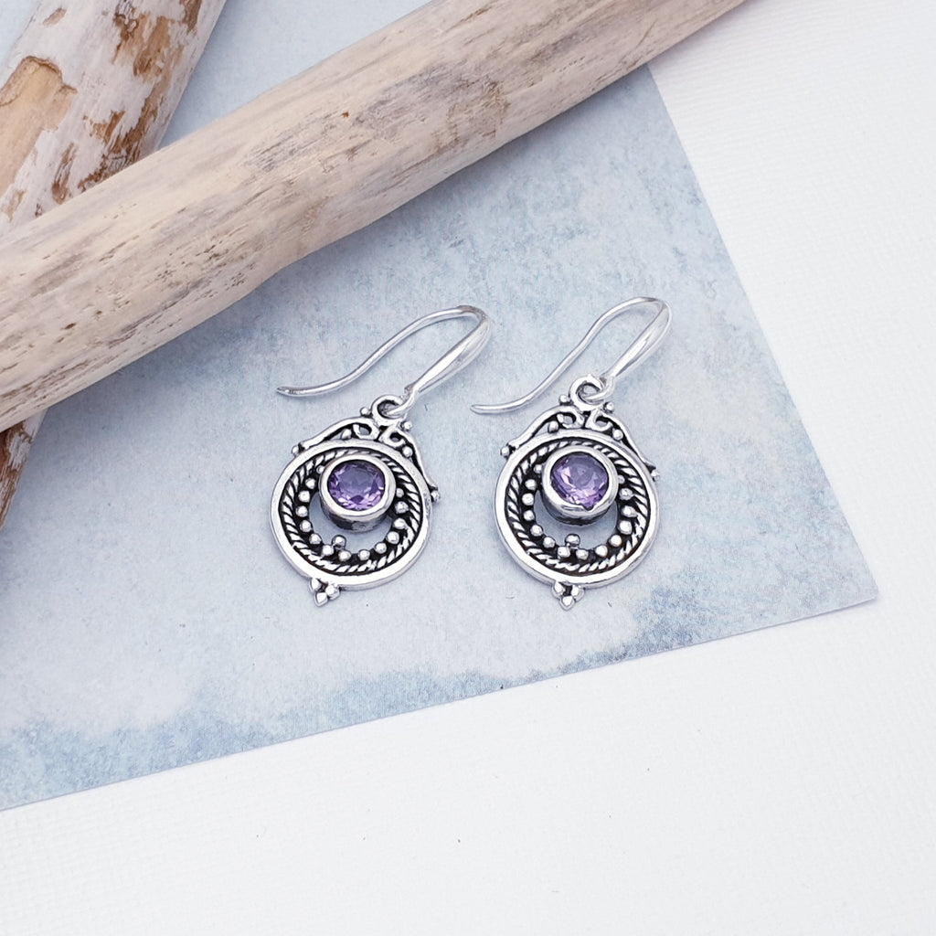 Each earring features a round, cabochon Amethyst stone in a simple setting. Intricate Sterling Silver detailing decorates around the stone, and is given depth and presence by the clever use of oxidisation. 