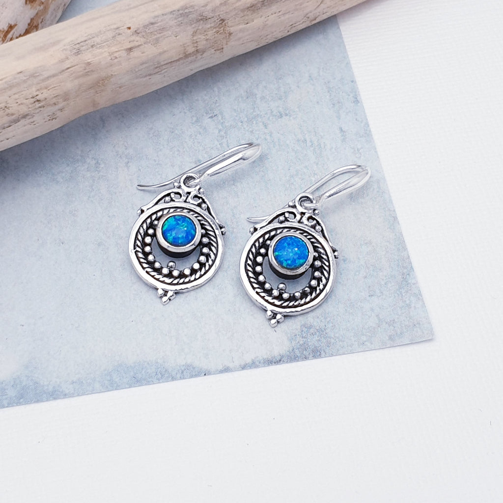 Each earring features a round, cabochon Reconstituted Opal stone in a simple setting. Intricate Sterling Silver detailing decorates around the stone, and is given depth and presence by the clever use of oxidisation. 
