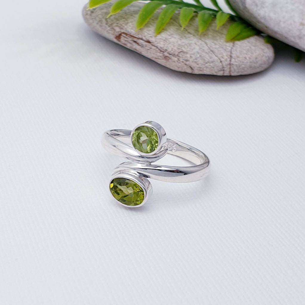 This beautiful ring features two tabletop cut, Peridot stones in Sterling Silver settings. One oval and one round stone, has been arranged one above the other. The band, gives this ring a wrap around feel, giving it that 'something a little different' we love so much at Silver Scene.