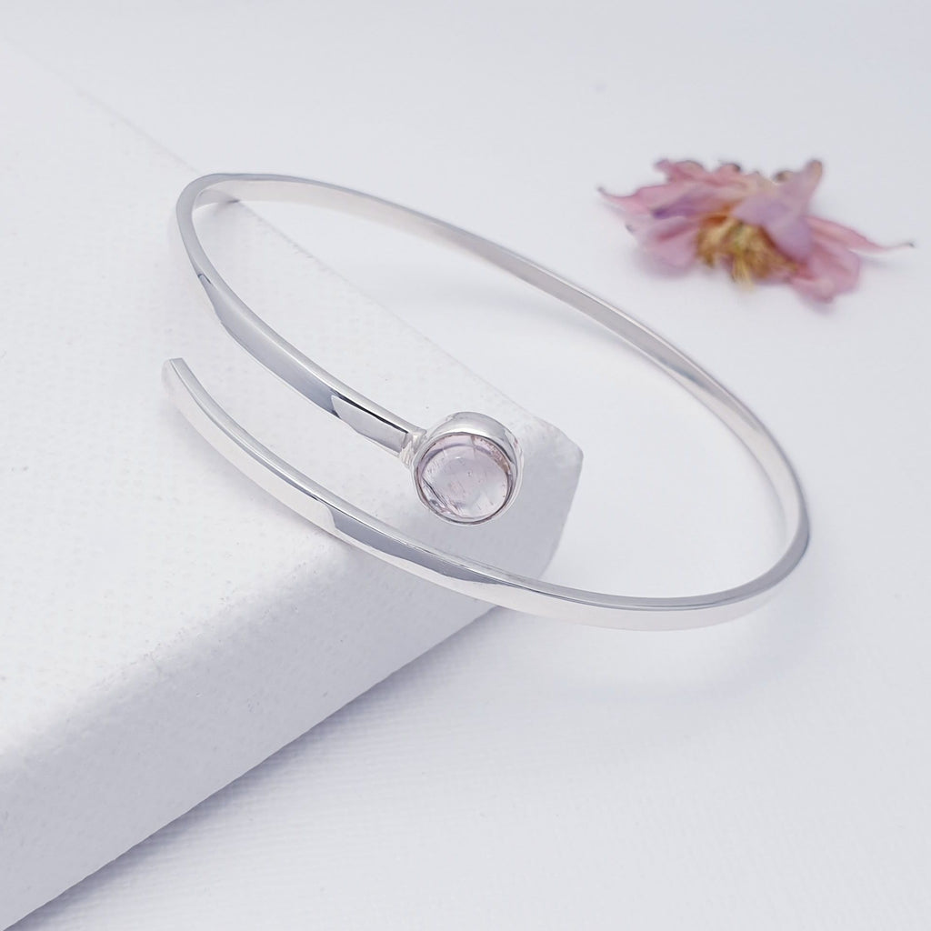 A simple design, this bangle features a round, cabachon, Pink Tourmaline stone in a simple setting. Compromising of a solid Sterling Silver bar that wraps elegantly around the wrist, it is perfect worn on its own or combined with other bangles and bracelets. This bangle is open at the front allowing a bit of movement and aiding when taking on and off the hand.