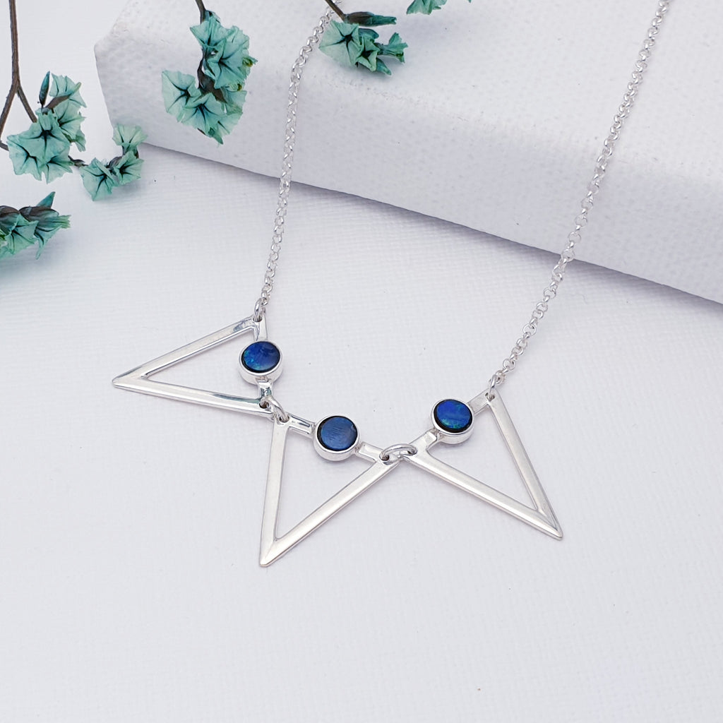 This beautiful necklace features three small round Australian blue Opal stones. Each stone sits at the top of a Sterling Silver cut out triangle with a larger triangle in the middle and two smaller triangles either side. A fine silver belcher chain has been used in this necklace and the extendable chain means that this necklace can be worn in lengths 16"-17" giving you peace of mind when buying as a gift. As a finishing touch, a small Blue Topaz bead decorates the end of the extension chain.