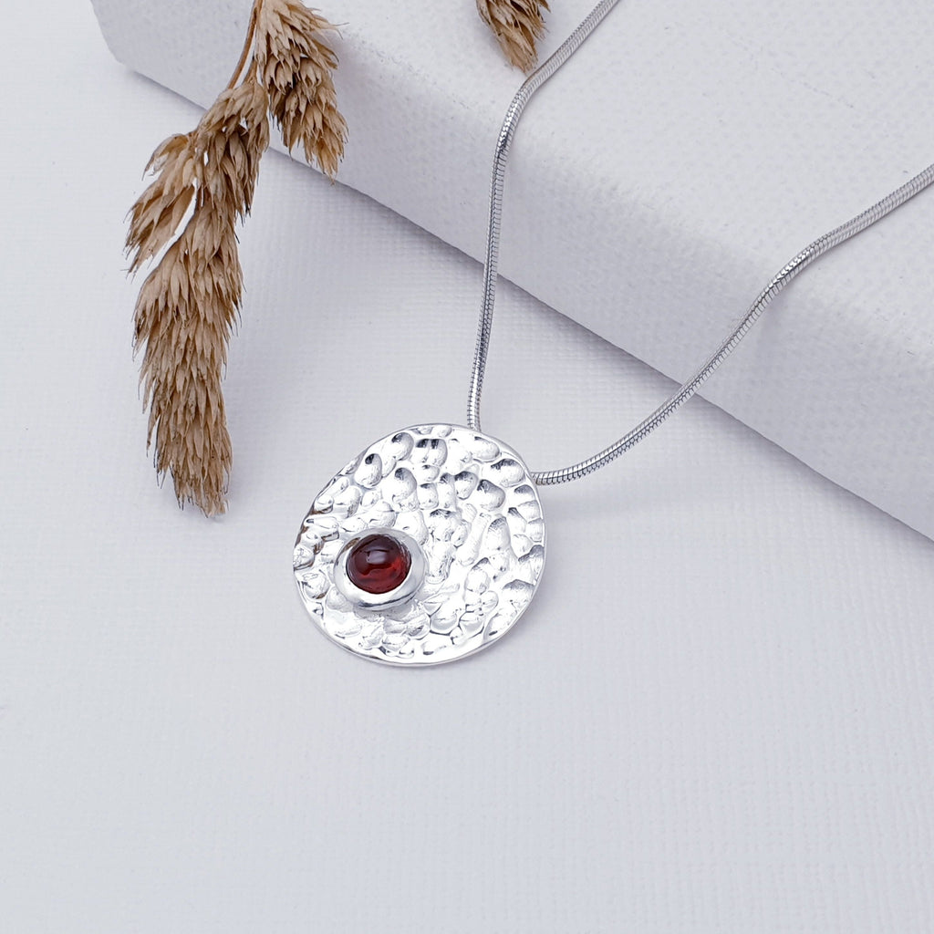 Our Garnet Sterling Silver Hammered Disk Pendant (chain not included) is so cute and would be perfect for everyday wear.  This stunning pendant features a small, cabochon Garnet sitting off-center on a beautiful, hammered Sterling Silver disk. This textured effect creates a stunning, reflective surface which catches the light as you move.